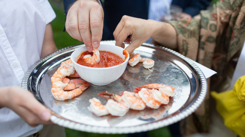 Hands dipping shrimp in cocktail sauce