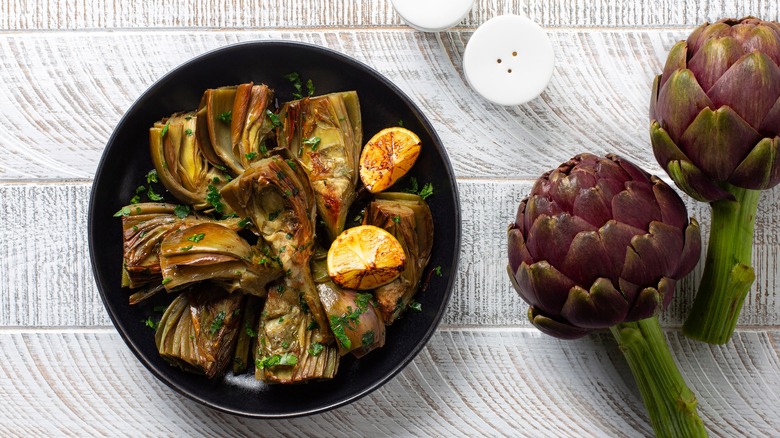 Grilled artichokes next to whole artichokes