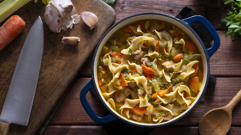 Crock of chicken noodle soup with vegetables, knife