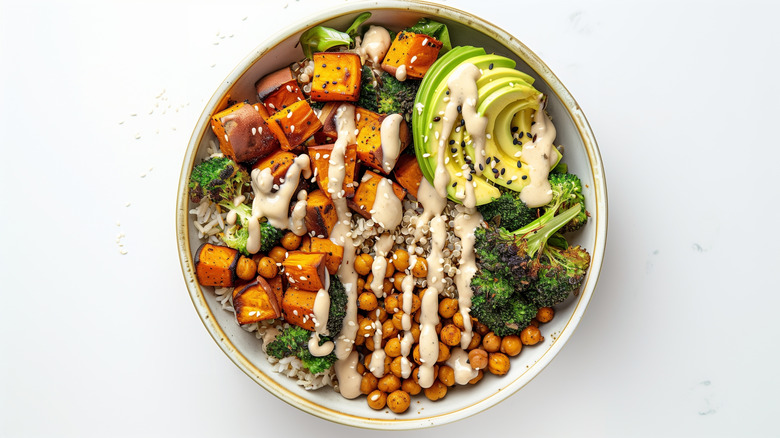 bowl of quinoa topped with roasted sweet potato, broccoli, avocado, sesame seeds, and tahini