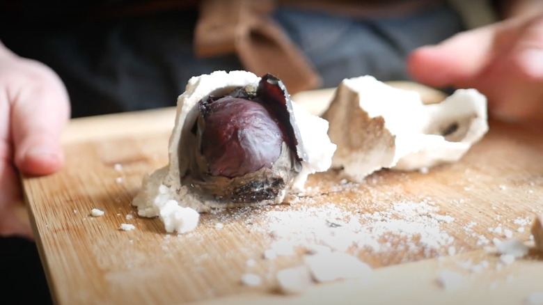 hands holding cutting board with beet encased in salt crust