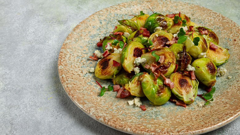 slow roasted brussels sprouts on a plate with crumbled cheese and bacon