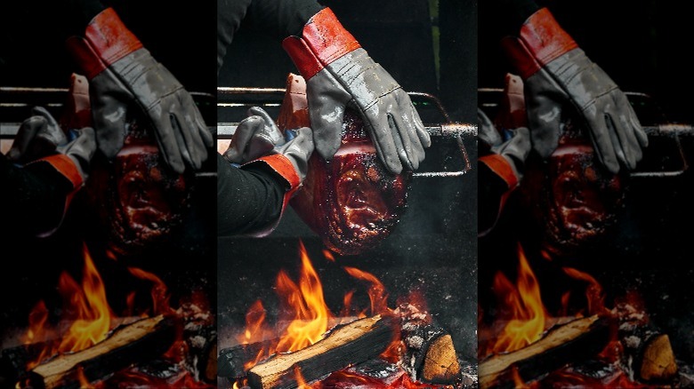 Gloved hands rubbing barbecue pork over flames