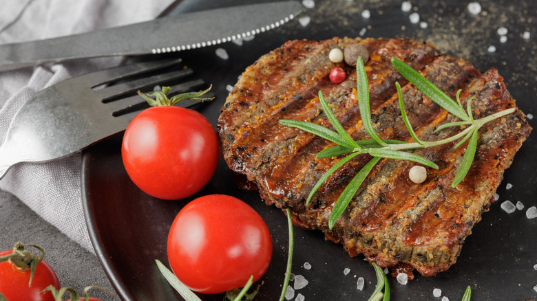 A seared eye of the round steak topped with rosemary, peppercorns, and served with tomatoes