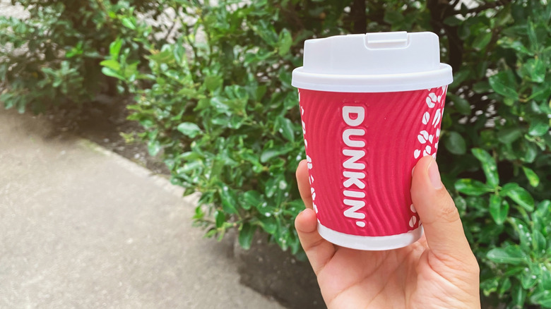 Person holding a Dunkin coffee cup outside by bushes