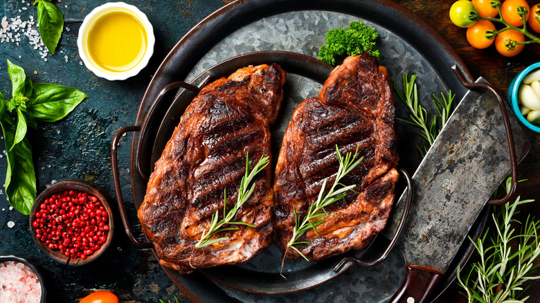 Two grilled ribeye steaks in a cast iron skillets surrounded by seasonings