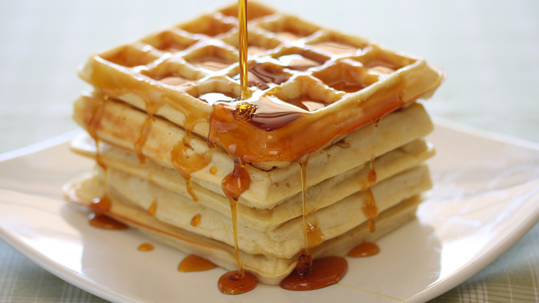 pouring syrup on stack of waffles