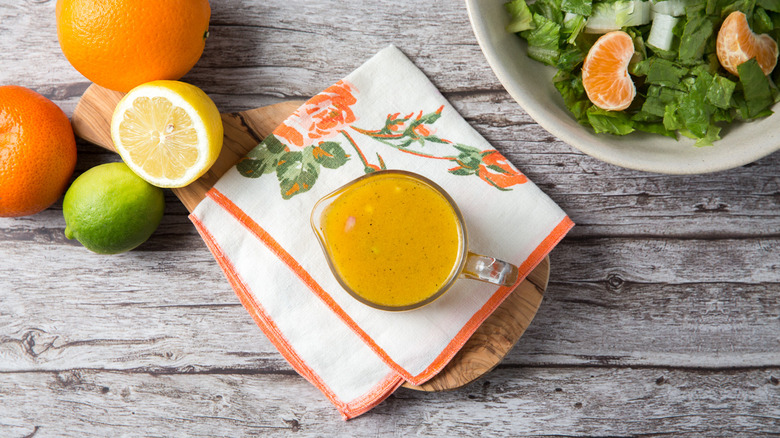 Citrus vinaigrette in serving cup next to citrus fruits and salad
