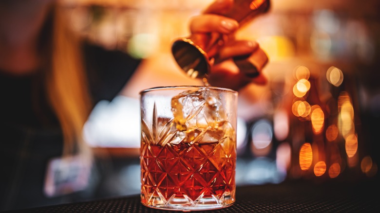 Bartender pouring negroni into whiskey glass