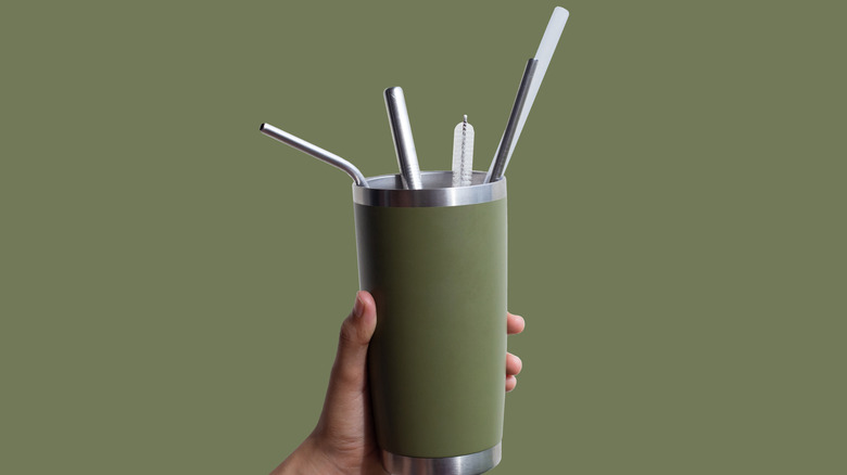 A hand holds up a green coffee tumbler with cleaning tools and a straw inside