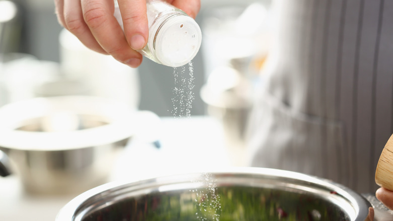 person adding salt to soup pot