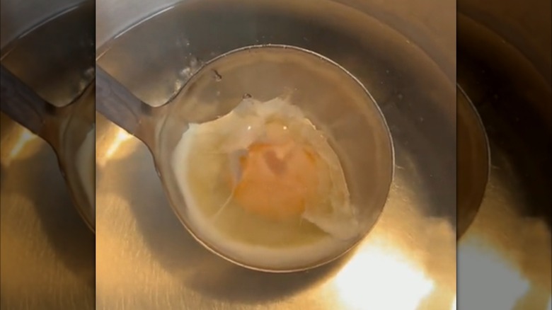 An egg poaching in a metal soup ladle