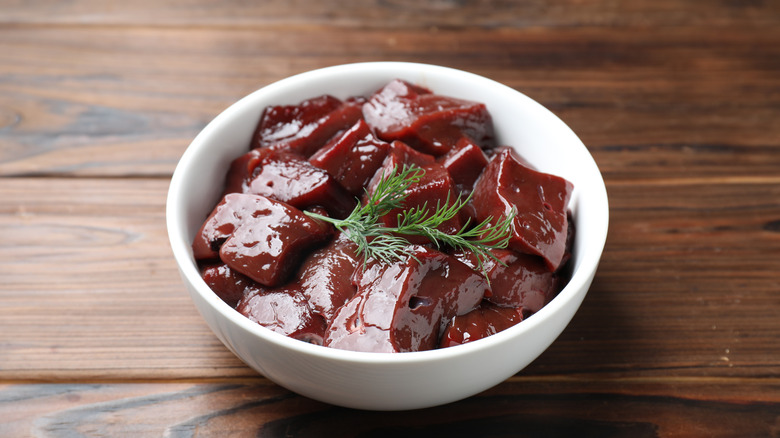 Bowl of raw chunks of beef liver in a bowl with a sprig of dill