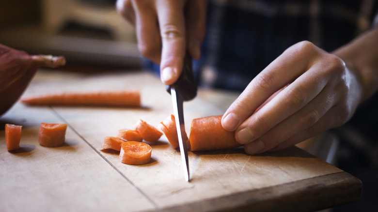 hands slicing carrots on a wooden cutting board