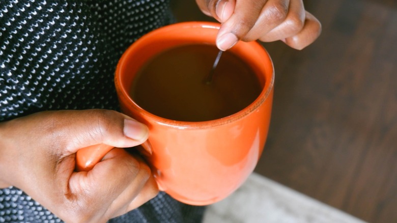 Hands holding and stirring a mug of coffee