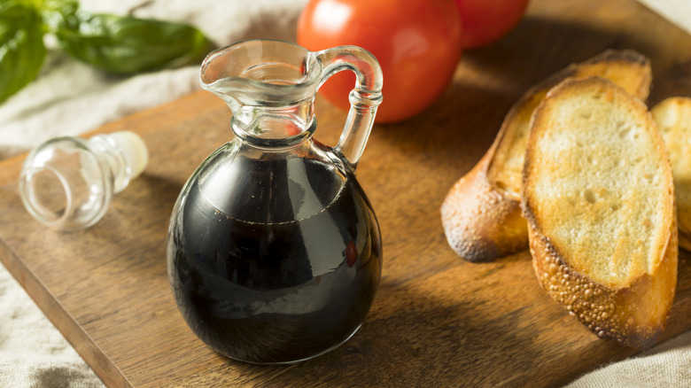 Glass carafe of balsamic vinegar on a board with toasted bread and tomatoes