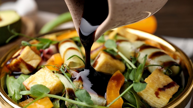 Pouring balsamic vinegar onto a salad with peaches and watercress