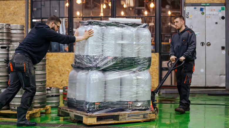 Two men moving kegs of beer on a pallet