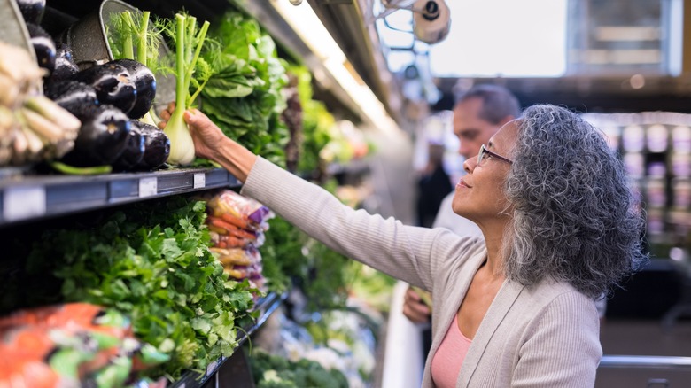 A woman investigating a bulb of fennel at a grocery store