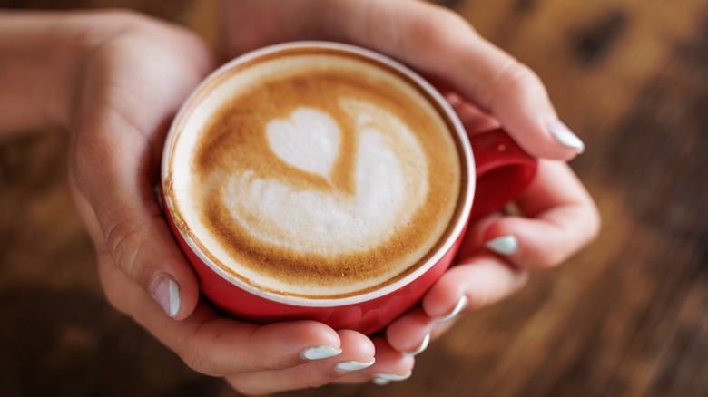 Hands holding a mug of coffee with latte art