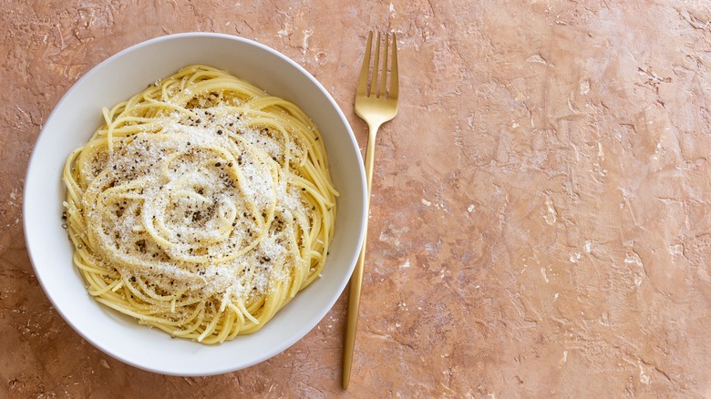 a bowl of cacio e pepe with a gold fork on a terracotta background