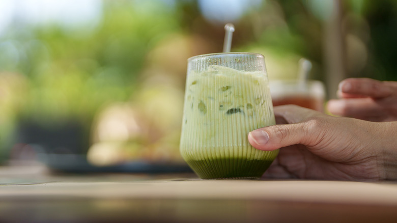 Hand holding iced matcha latte outdoors