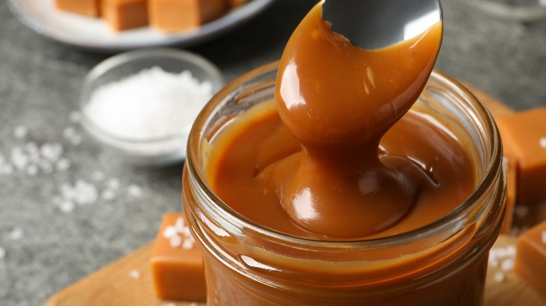 Close-up of a spoon dipping into a jar of caramel 