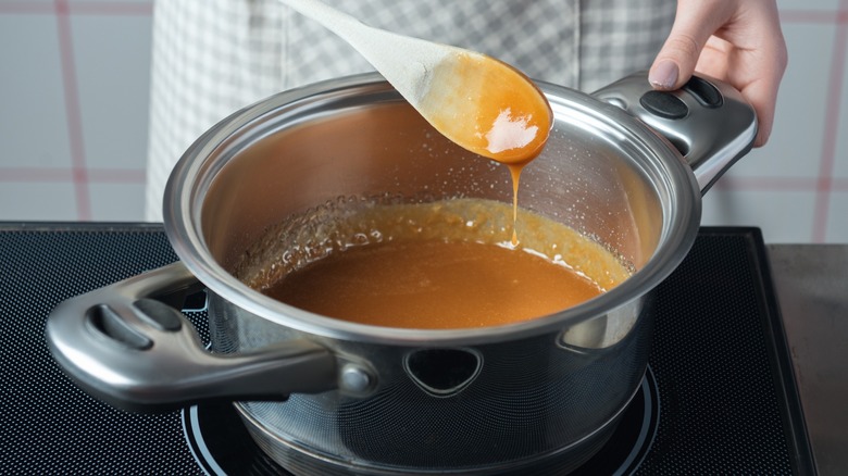 Hand holding a wooden spoon over caramel in a pot on a stovetop