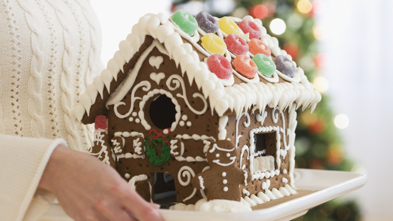 Person holding a decorated gingerbread house