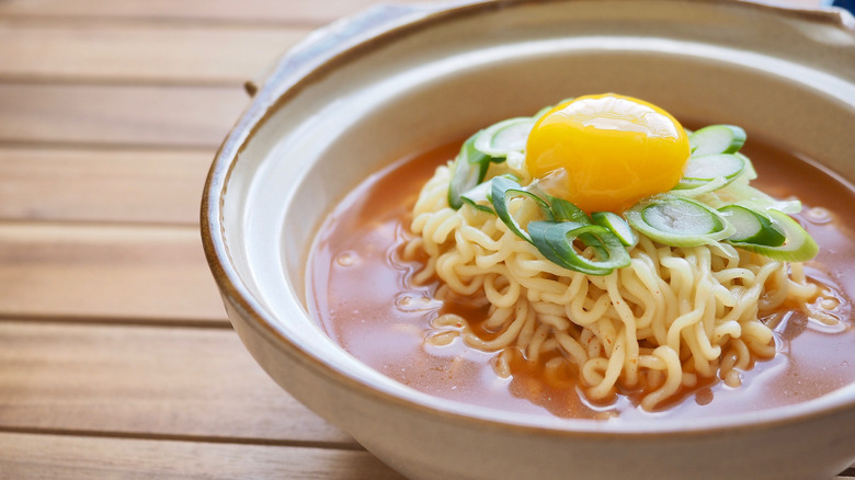 instant ramen wiht a cracked egg in a bowl on a wood surface