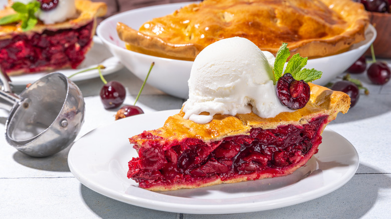 slice of cherry pie with ice cream on white plate