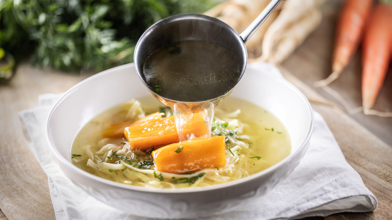 Ladling vegetable and noodle soup into bowl