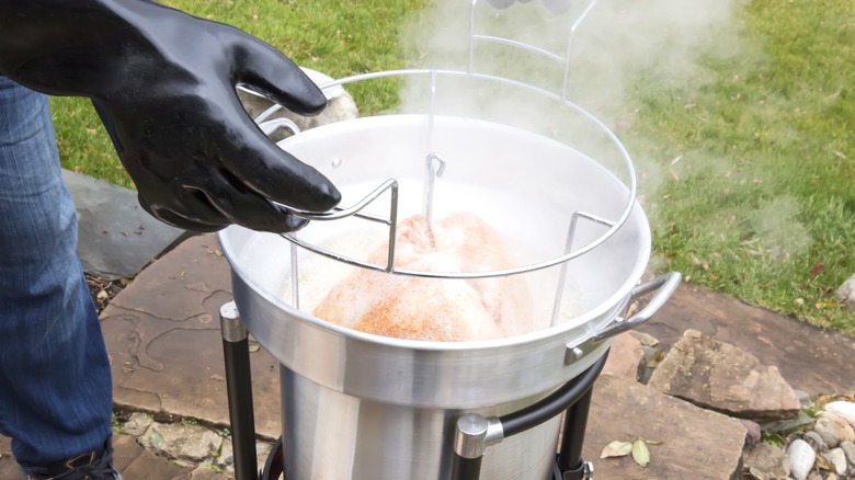 Gloved hands deep frying a turkey outdoors