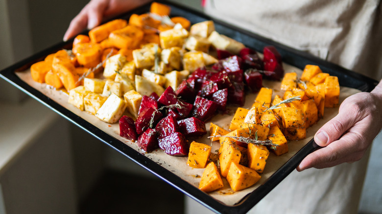 hands holding a baking sheet with assorted root vegetables for roasting 