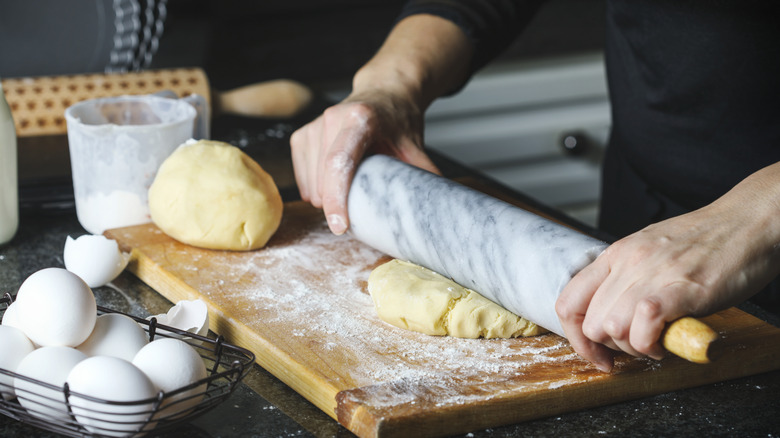 Hands rolling pie dough on cutting board