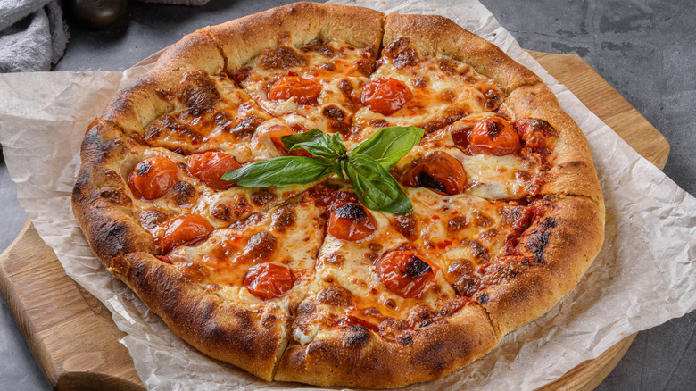 freshly baked pizza with tomatoes and basil leaves on wood board