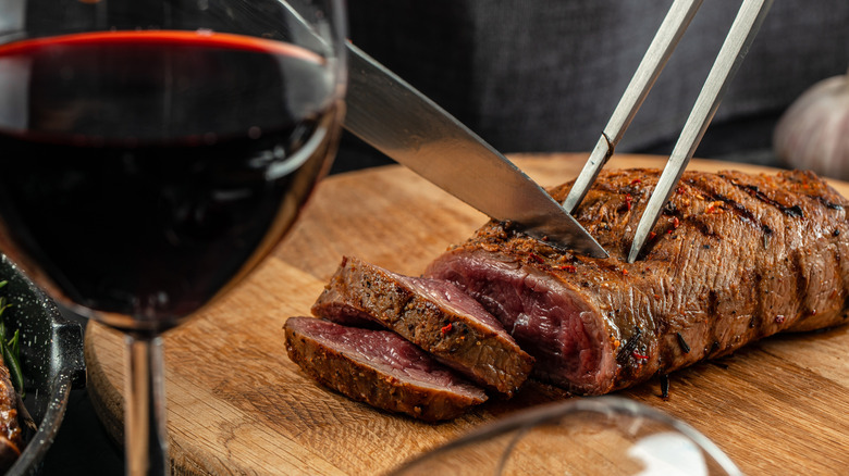 a steak being cut next to a glass of red wine