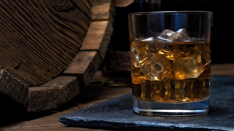 A glass of whiskey next to a barrel