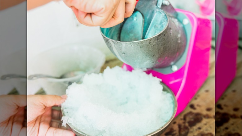 A hand using a machine to make shaved ice