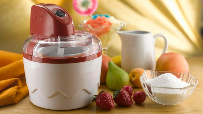 An ice cream maker with fruit and a bowl of sugar