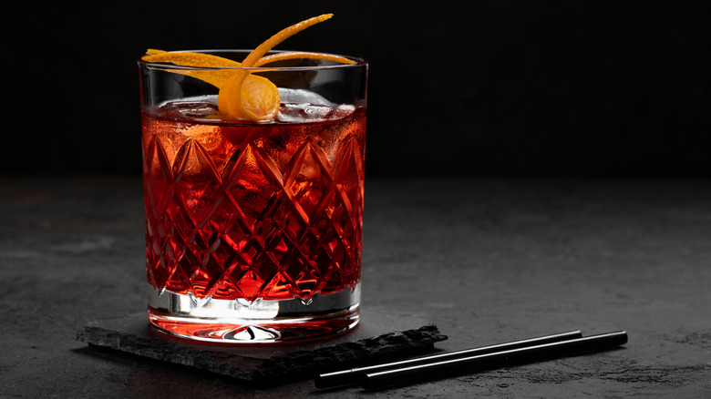 Negroni cocktail in lowball glass on black surface with straws