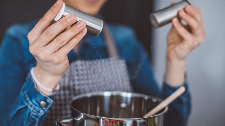 Woman holding salt and pepper over pot