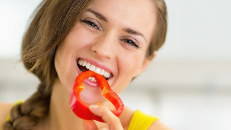 Smiling woman eating a slice of red bell pepper