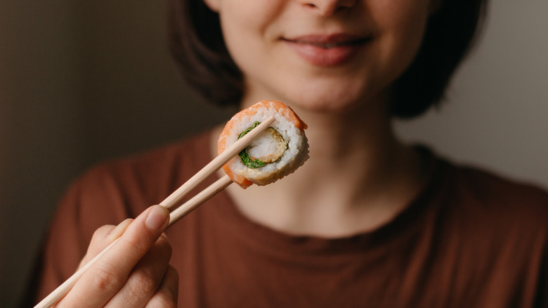 woman holding sushi in chopsticks