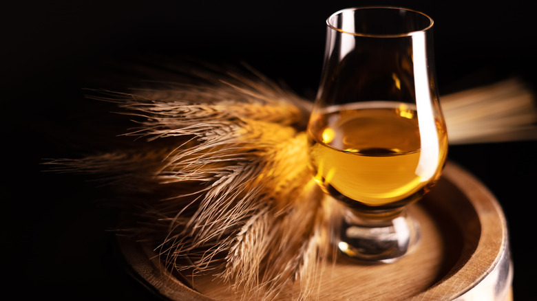 Glass of whiskey beside grain on an oak barrel