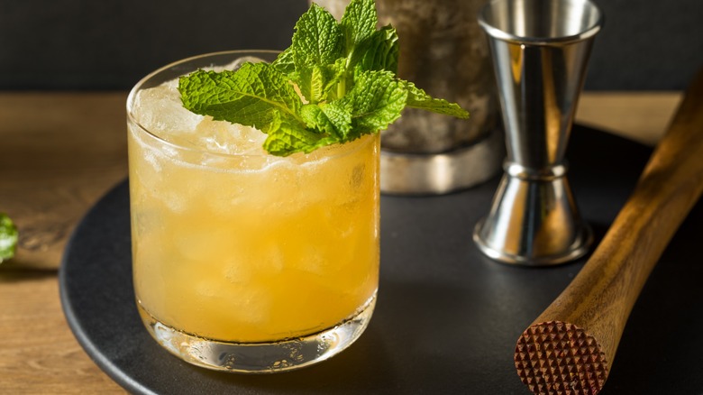 A whiskey smash cocktail garnished with mint next to a muddler