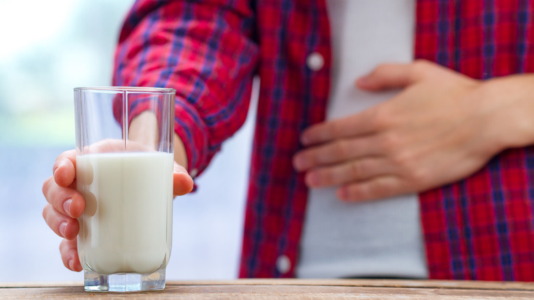 person holding stomach with glass of milk