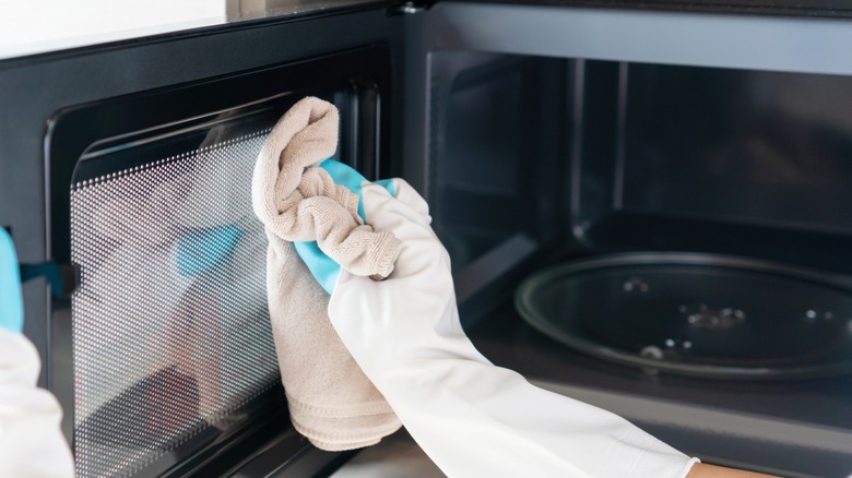 hand with towel cleaning microwave 