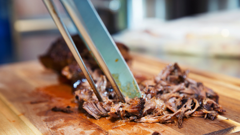 pulled pork on cutting board with tongs