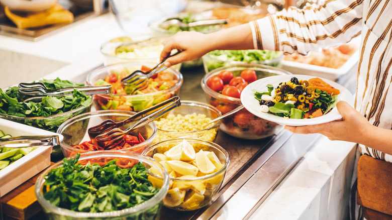 Person picking from bowls of ingredients at a salad bar